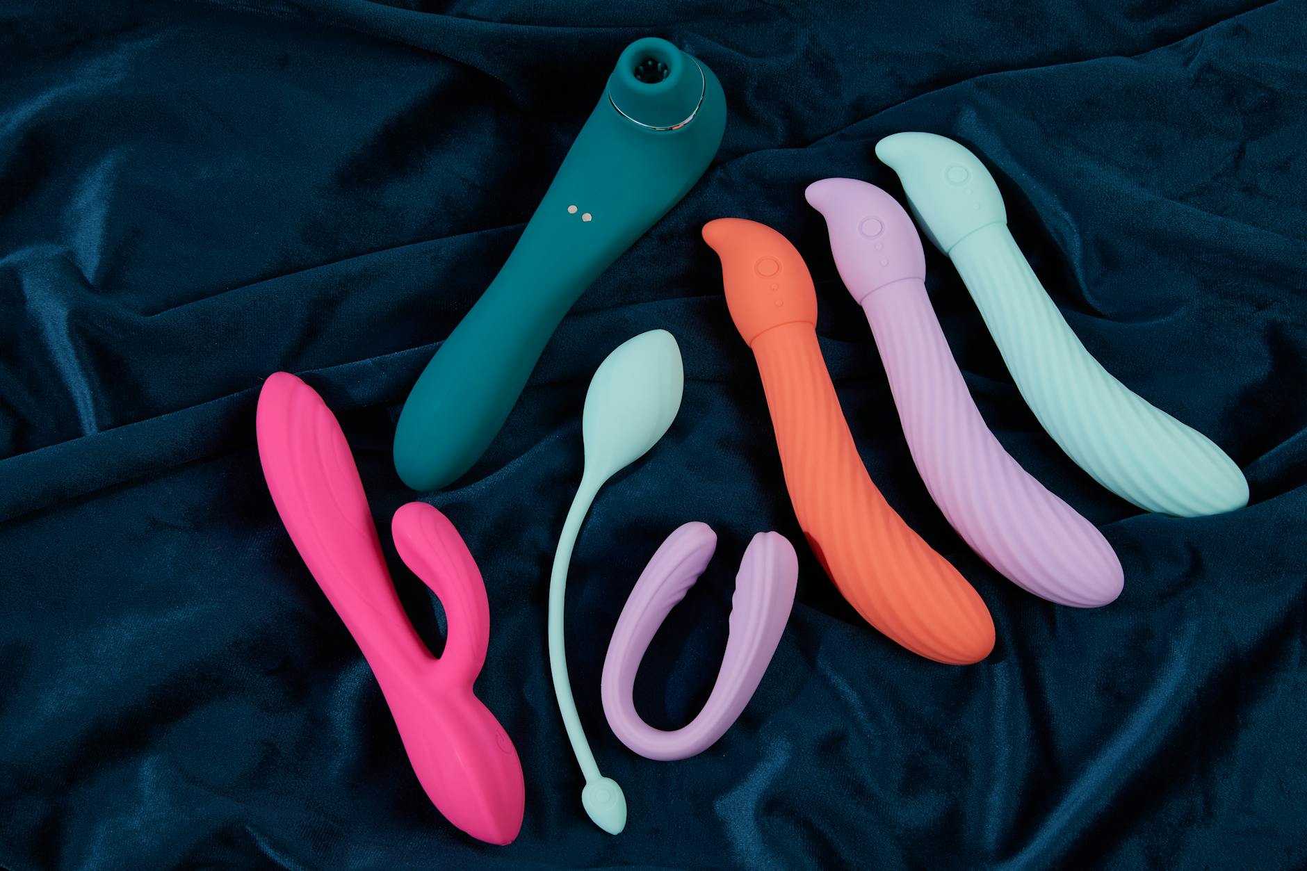 Woman holding blue and pink vibrators with contemplative focus, symbolizing pleasure exploration after body changes