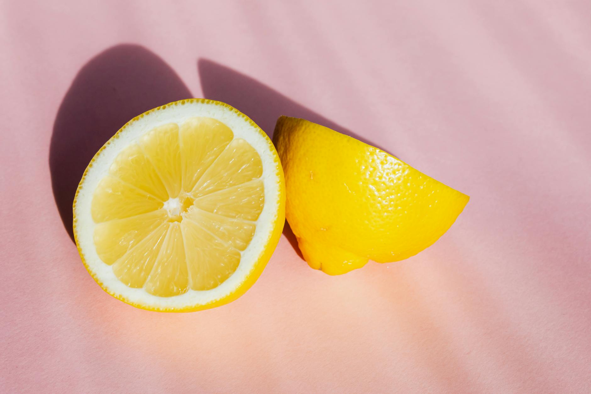 Fresh lemon halves on a pink background with soft sunlight