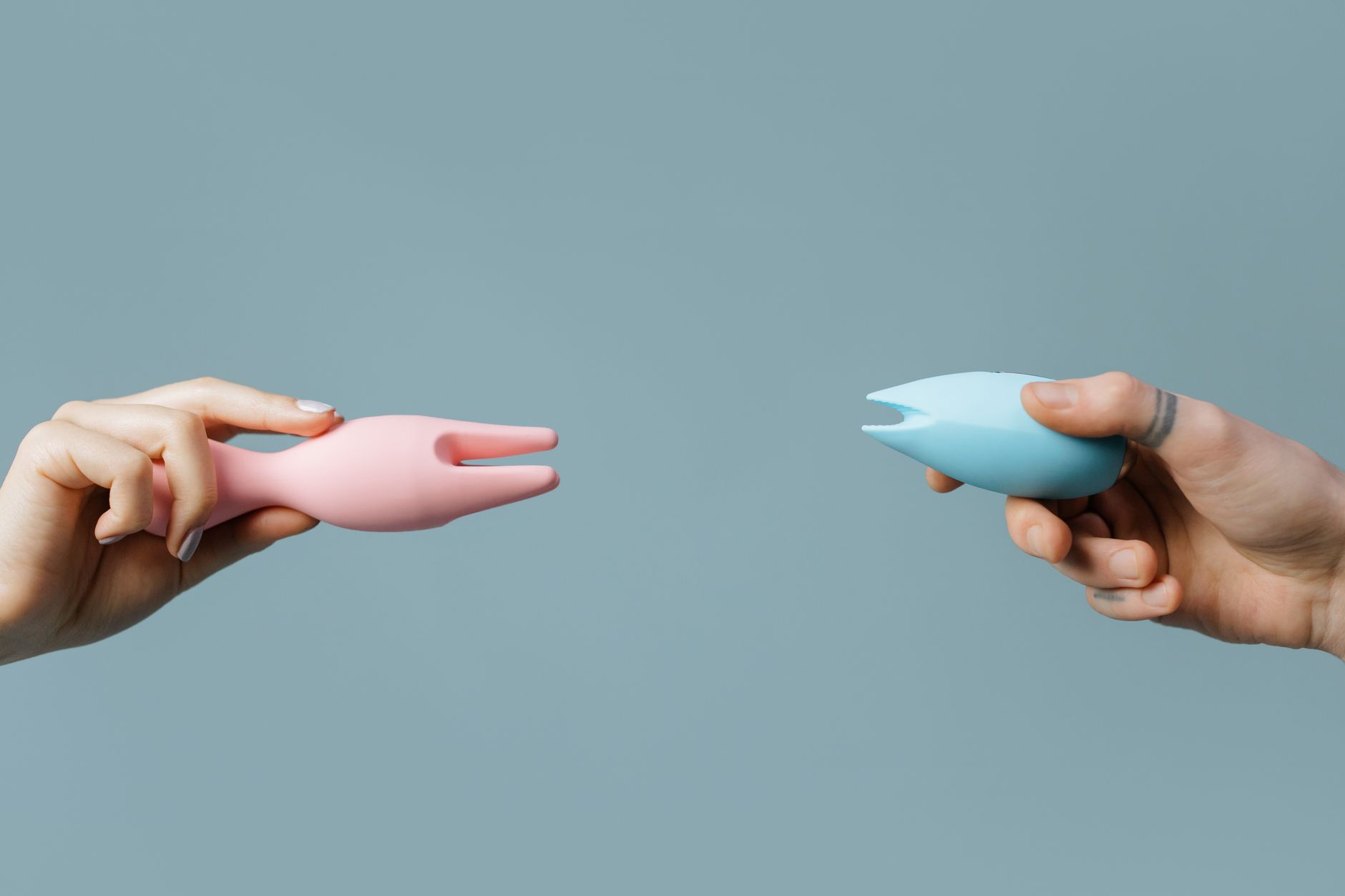 Woman holding blue and pink clitoral vibrators in a contemplative expression