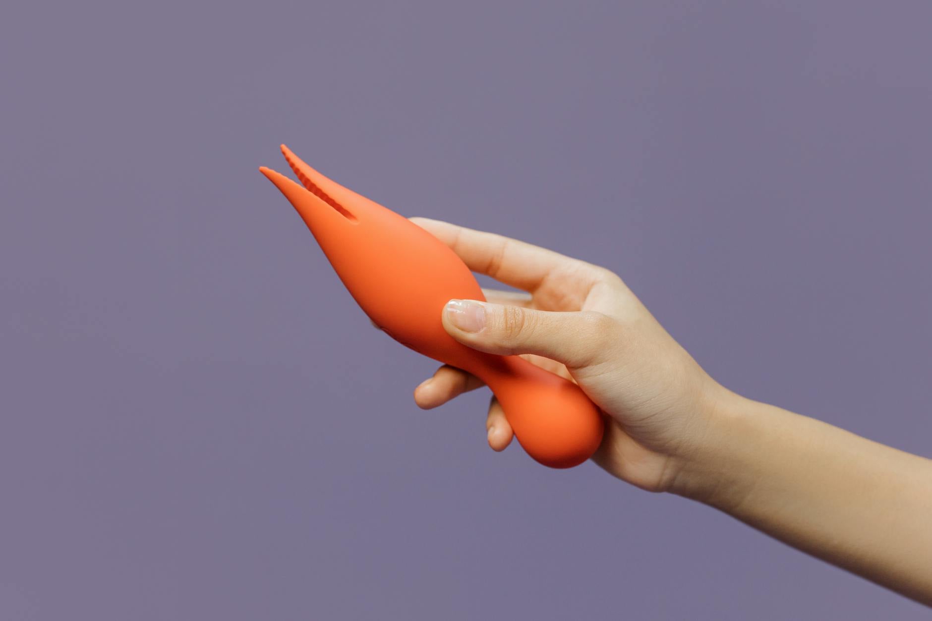 Hand holding an orange vibrator against a minimalistic purple backdrop, showcasing modern sensuality.