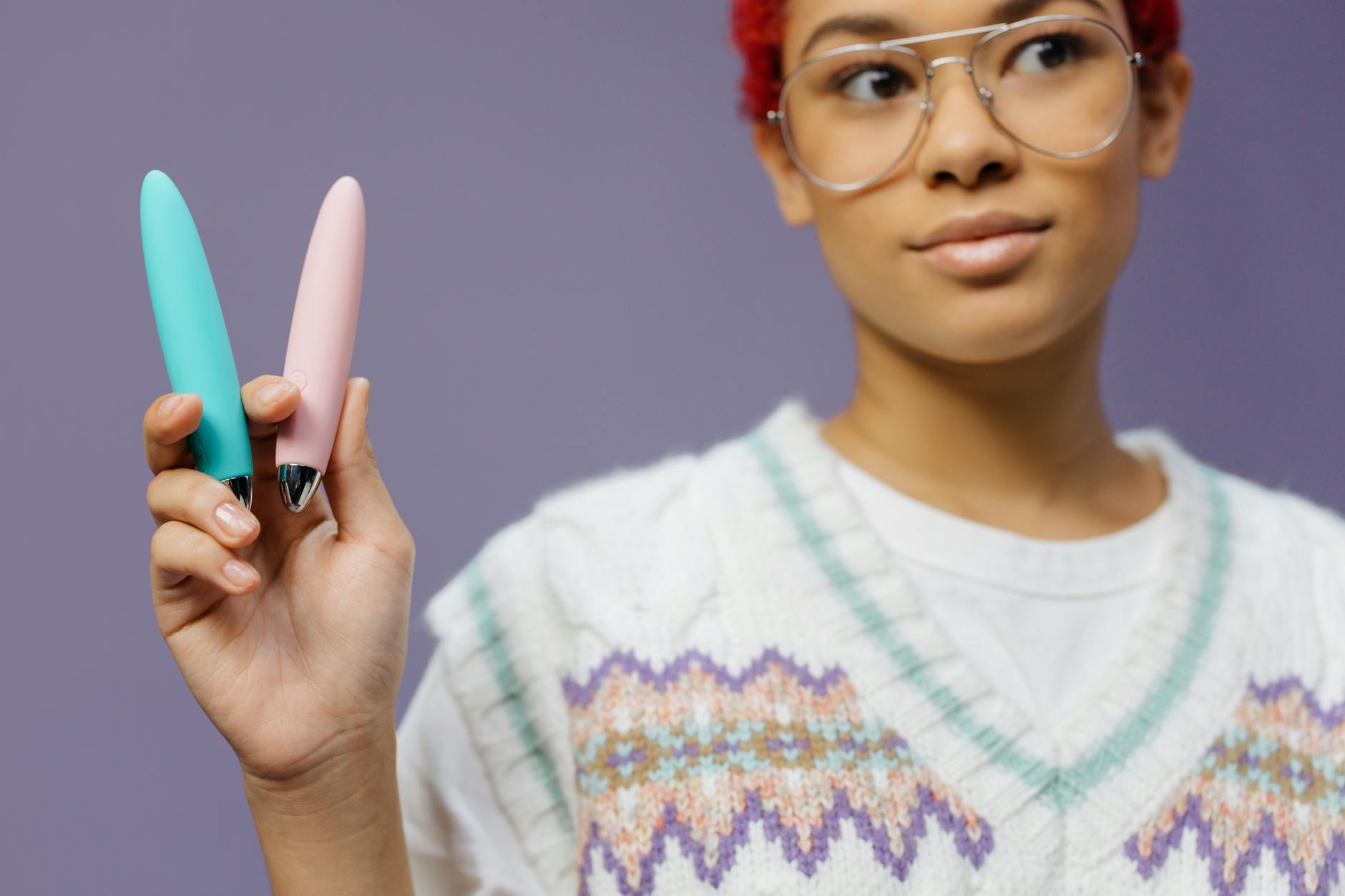 Woman holding colorful vibrators against a purple background, representing fresh starts and choice