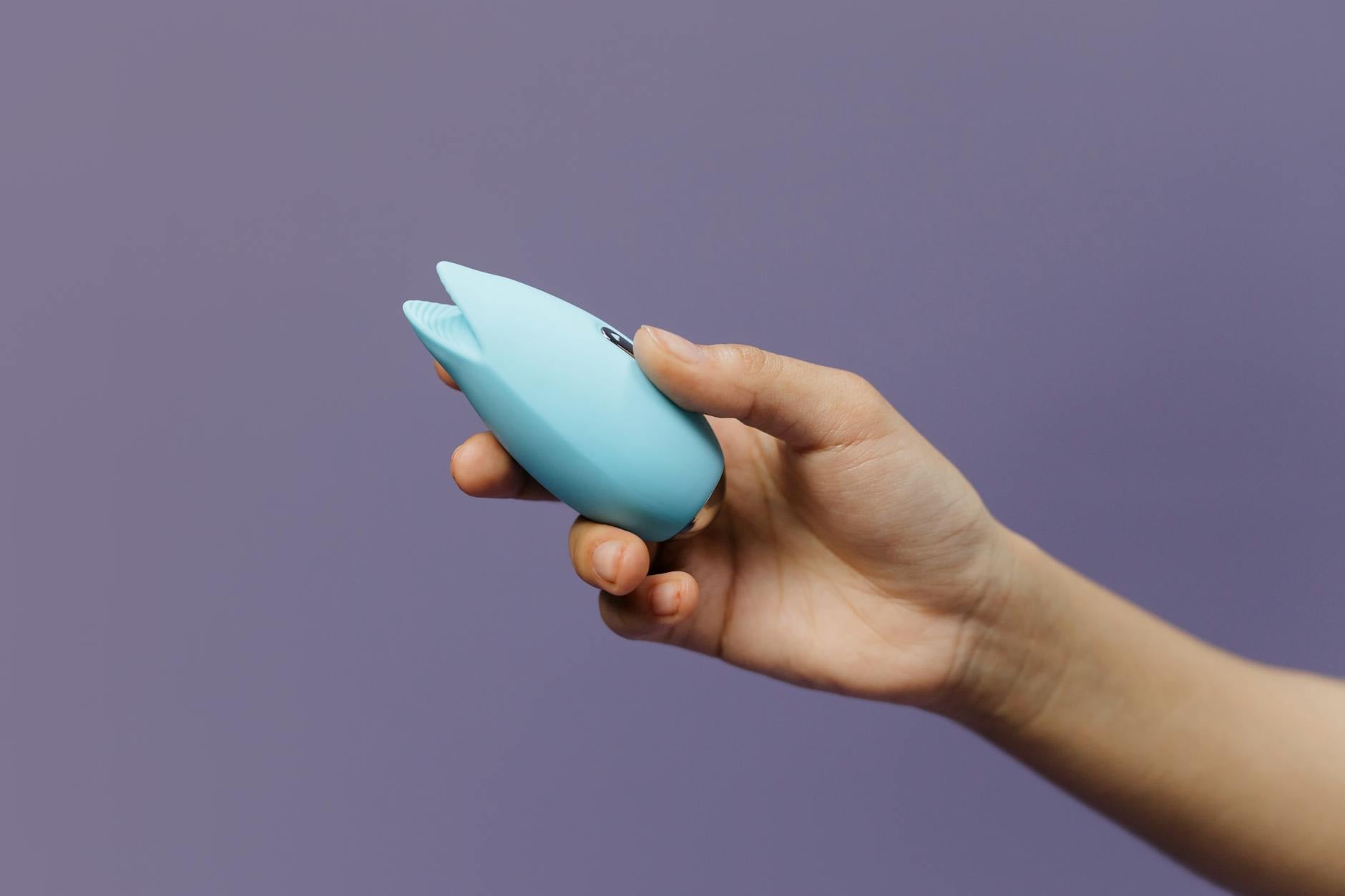 Hand reaching for a collection of colorful clitoral vibrators on a wooden table
