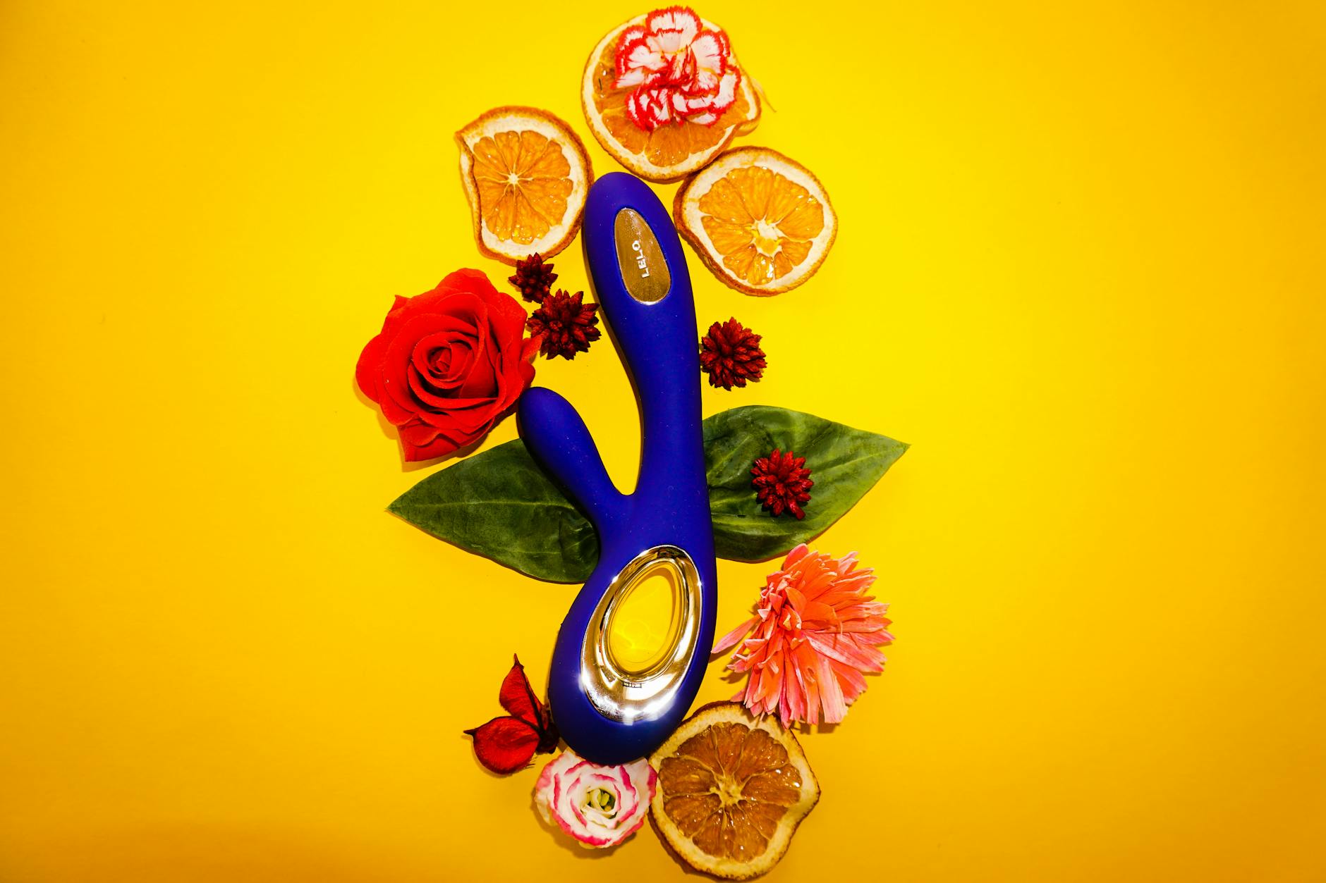 A blue clitoral vibrator surrounded by fresh lemons and citrus slices on a sunny yellow background.
