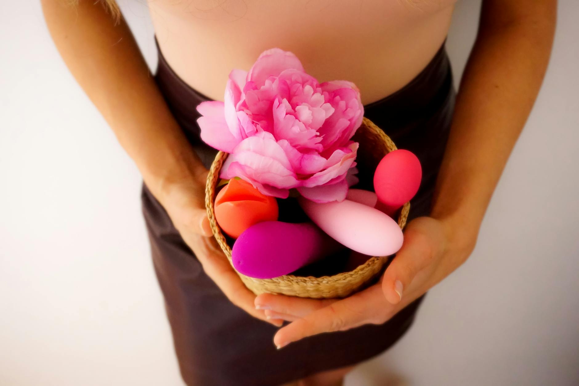 Woman with glasses holding blue and pink vibrators in contemplative expression